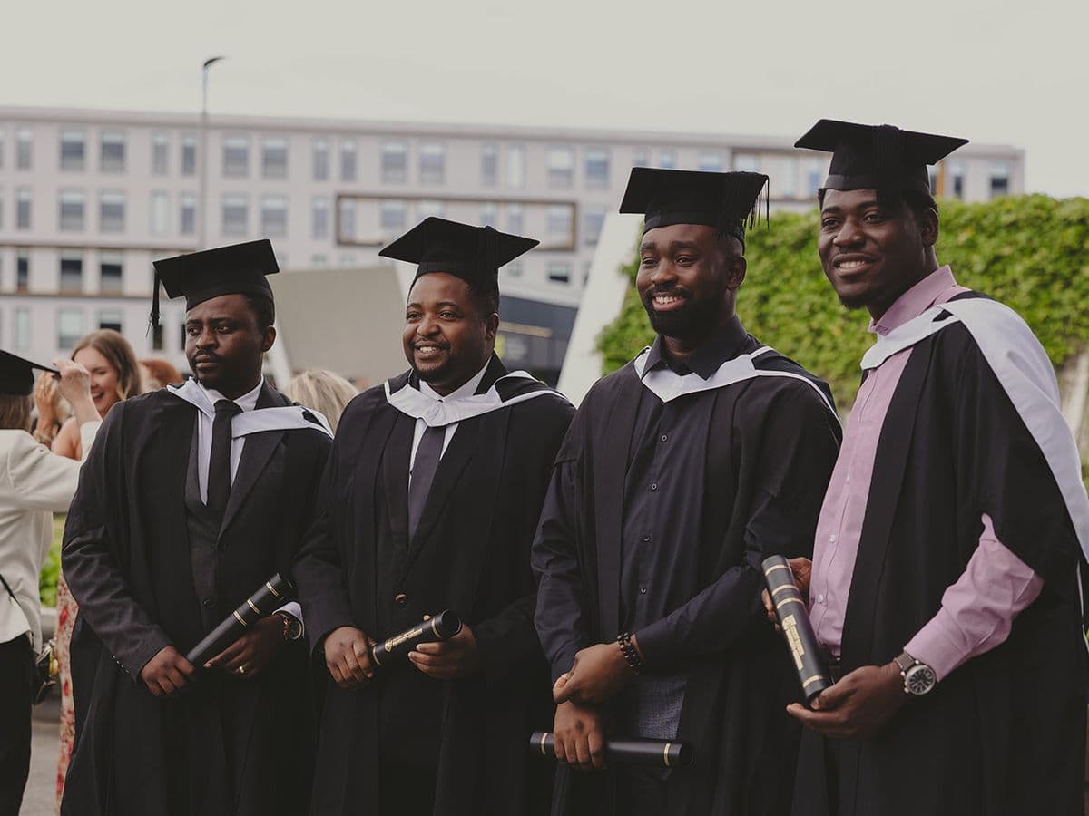 Four graduates in gowns and caps holding their diplomas outside a UK university